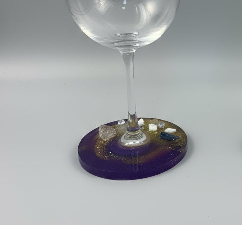 Clear wine glass on a purple coaster with decorative elements on a gray background
