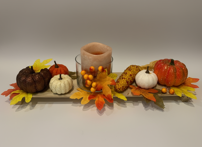 Decorative fall arrangement with pumpkins, leaves, and a candle on a white background